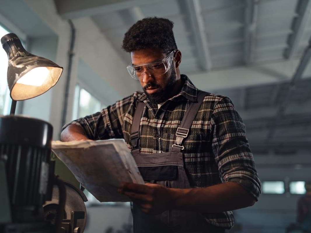 An industrial worker in protective gear reviewing documents in a factory setting